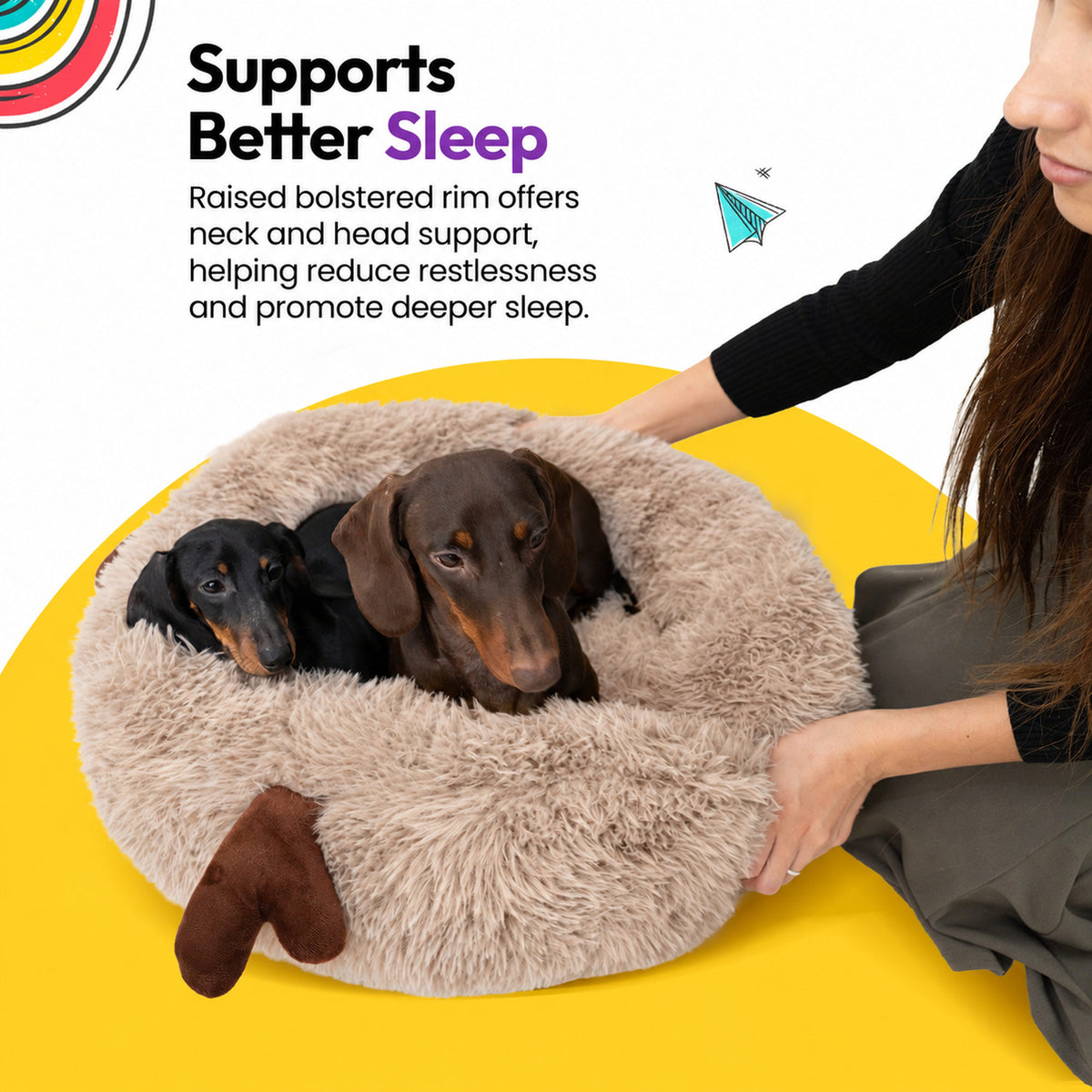 Cream | Fluffy Shag Calming Round Bed with Antlers: Two dachshunds lying in the bed while a woman strokes its rim, on a yellow graphic card