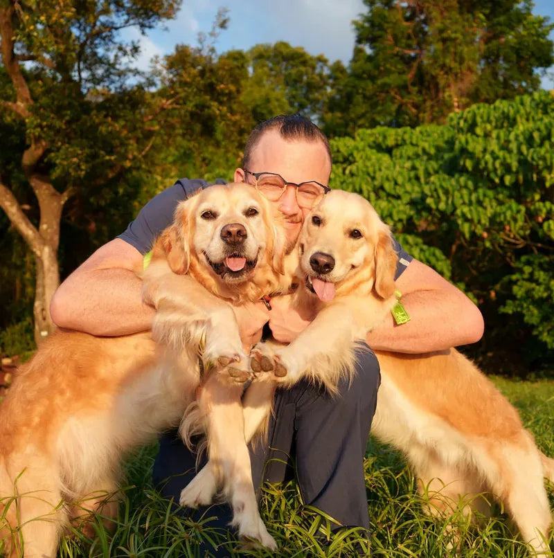 Dr Duncan Houston hugging his two Golden Retrievers, Bridie and Kiko, in a sunlit field